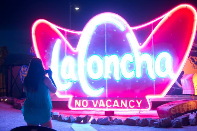 A woman takes a photo of the "La Concha" sign during a night tour at The Neon Museum, Monday, July 1, 2013.